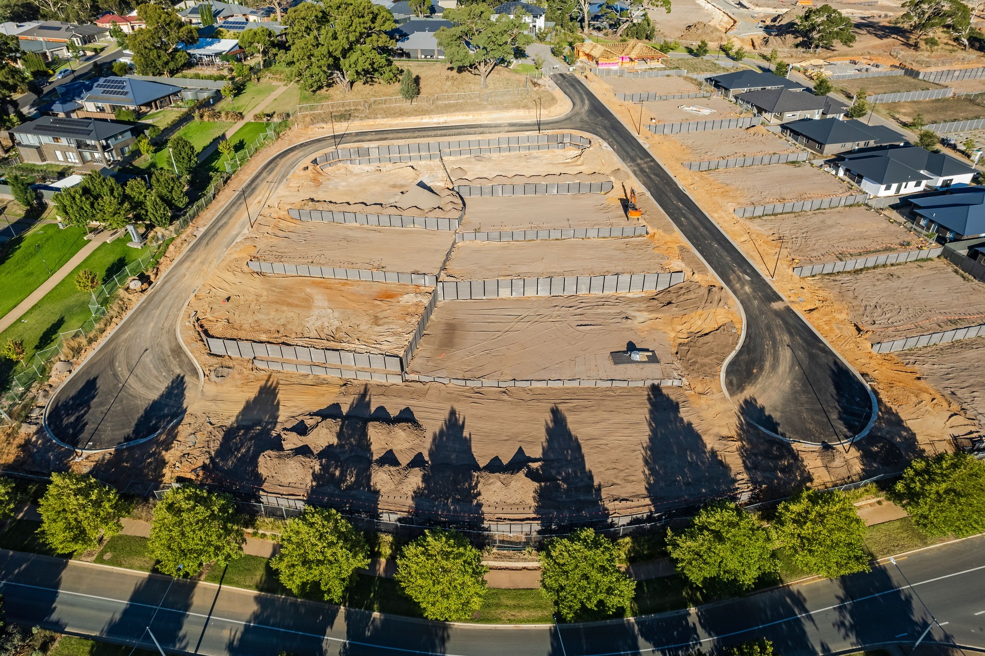 Aerial view new rural housing development earthworks, retaining walls, access roads with display homes and late afternoon shadows
